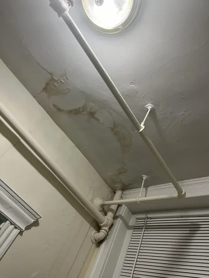 Water stains running across a ceiling beside an old heating pipe