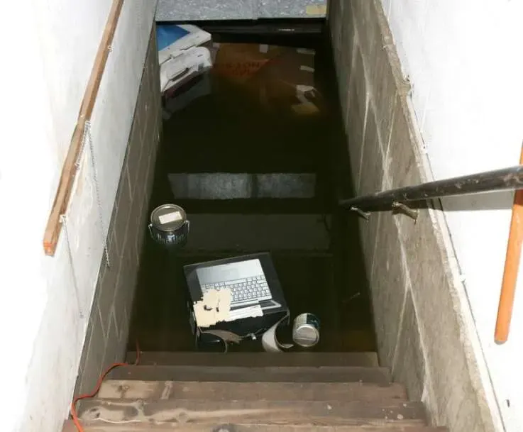 Floodwater filling a basement stairwell with belongings floating at the bottom