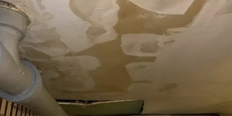 Water-stained ceiling with peeling paint below a leak from the floor above